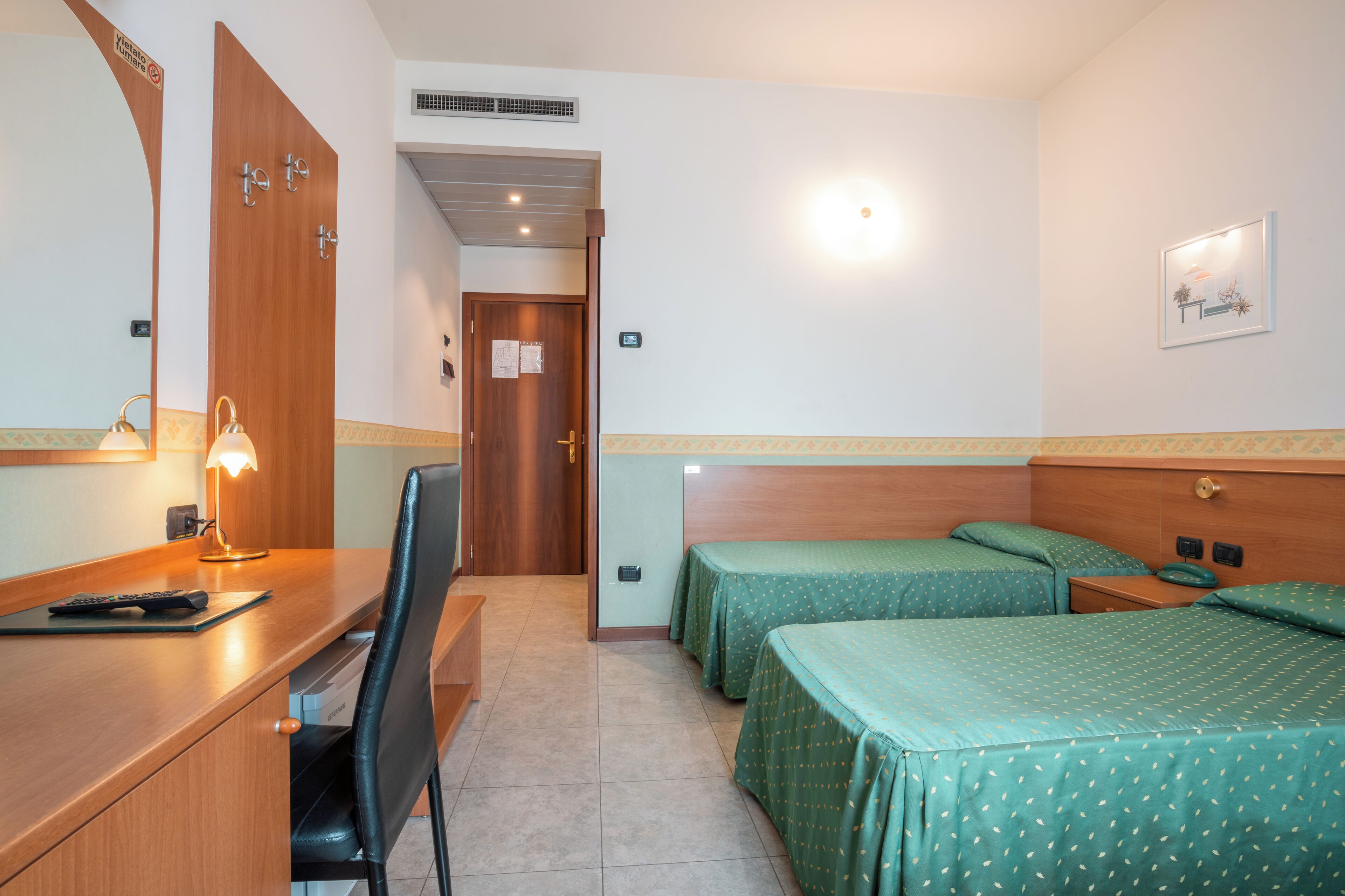 Una camera d'albergo con una scrivania, due letti singoli, una sedia e uno specchio.
