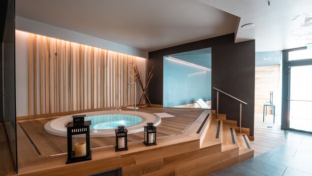 A modern spa area with a wooden floor, a circular hot tub, and three black lanterns.