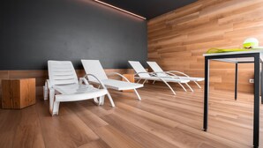 A modern room with wooden flooring, white lounge chairs, and a table with a lamp.