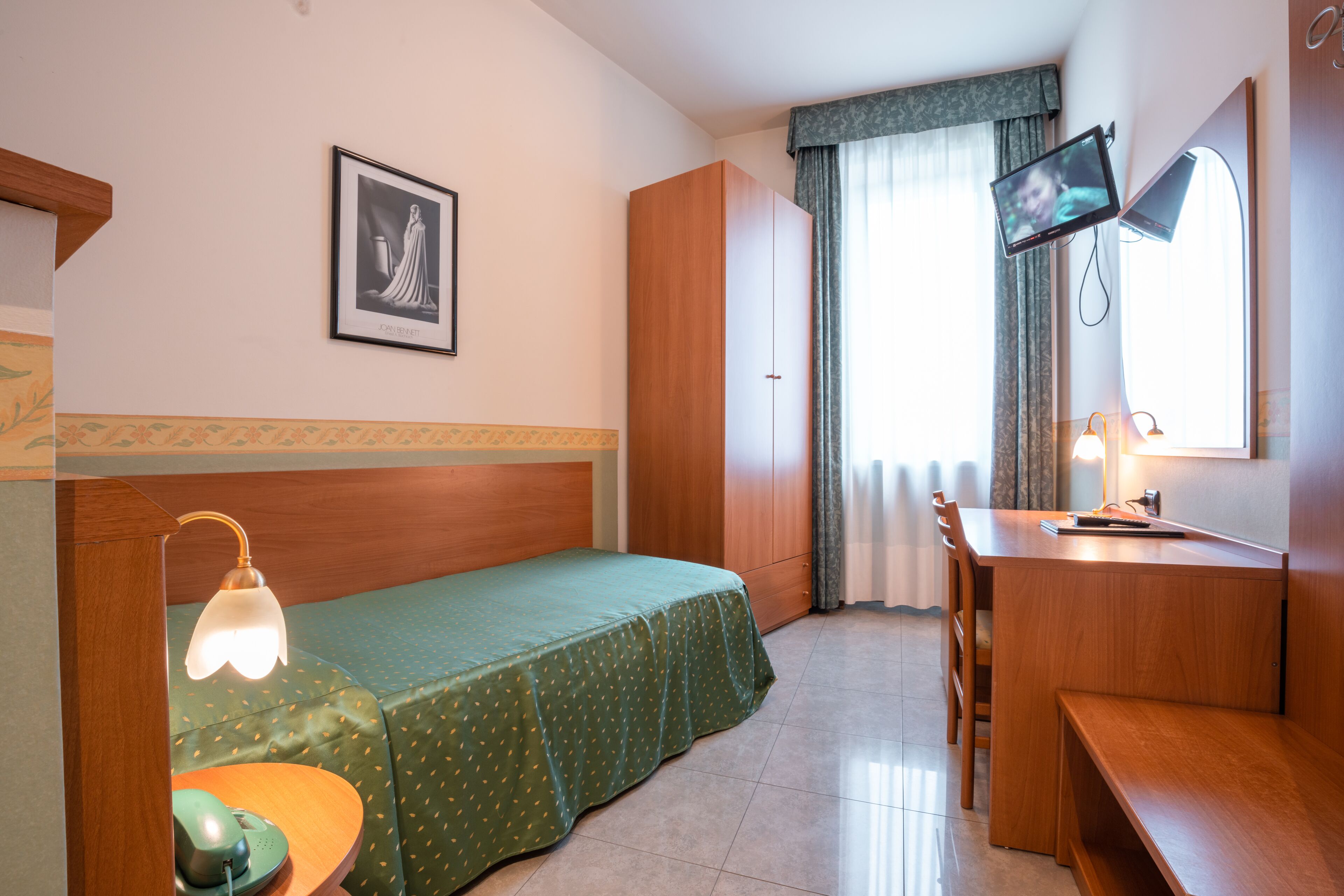 A hotel room with a bed, a desk, a chair, a television, and a window with curtains.