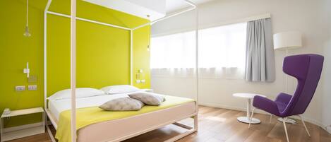 A modern bedroom with a four-poster bed, a bright green wall, a purple chair, and a small round table.