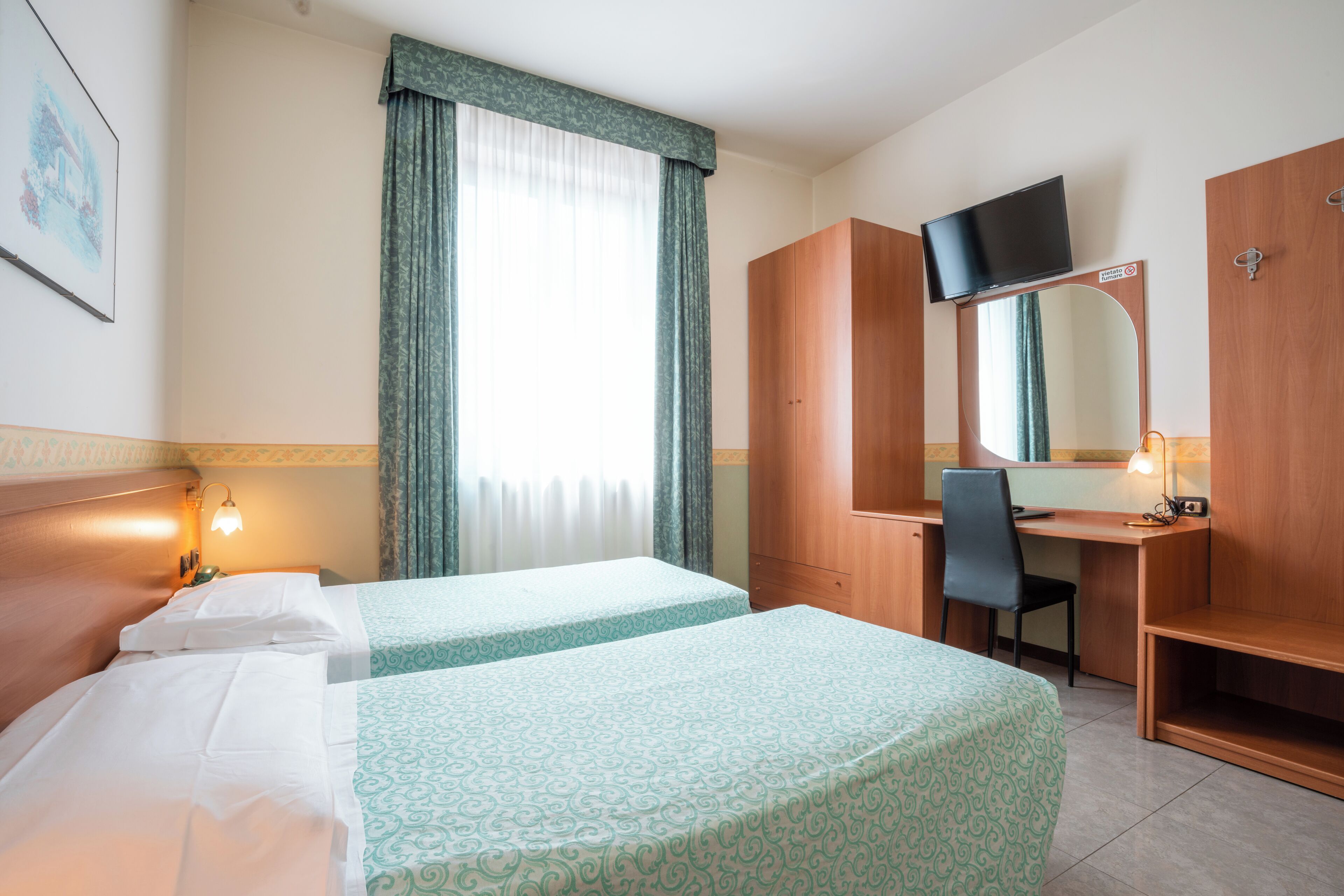 A hotel room with two beds, a desk, a chair, a TV, and a mirror.