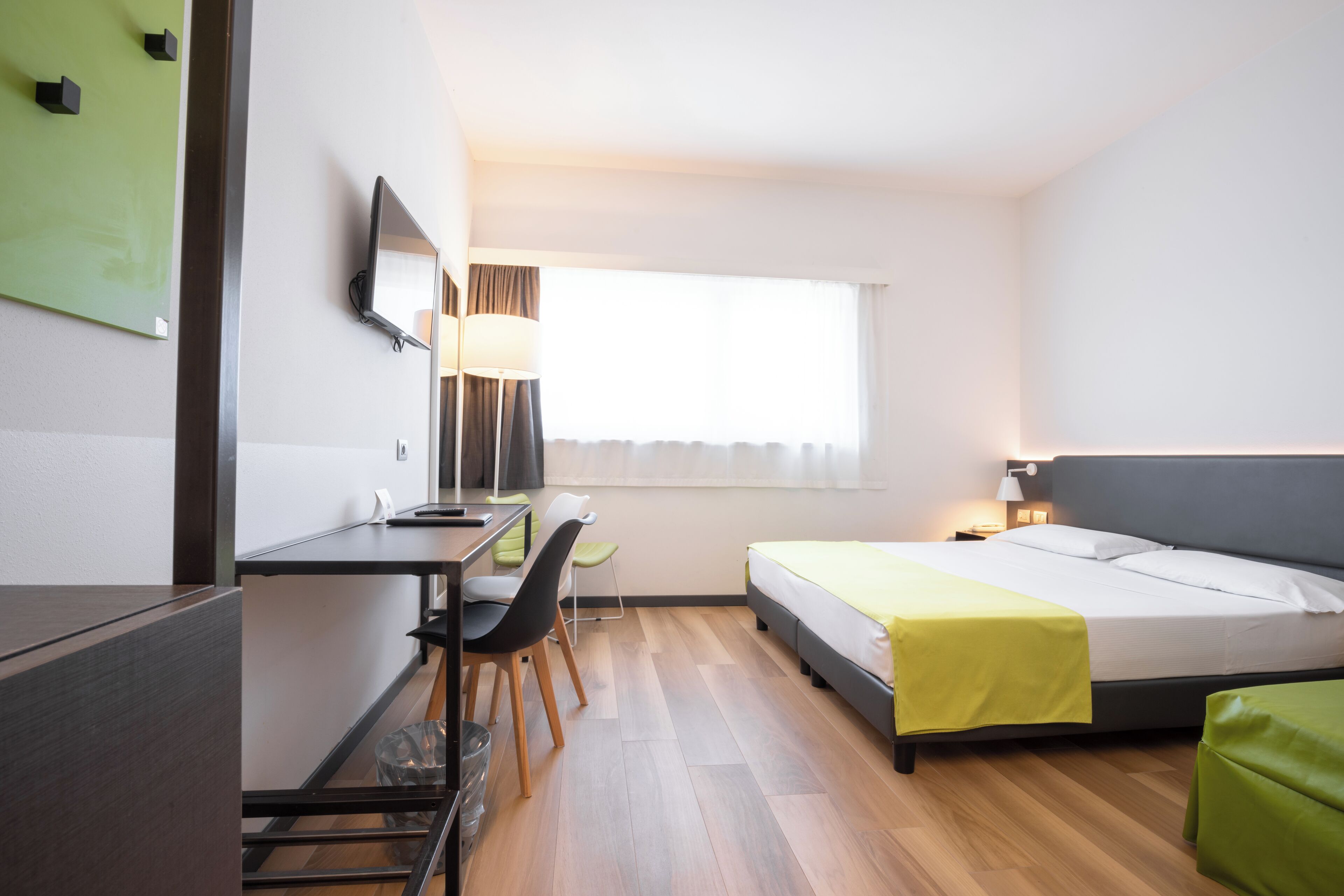 A hotel room with a bed, desk, chairs, and a television.