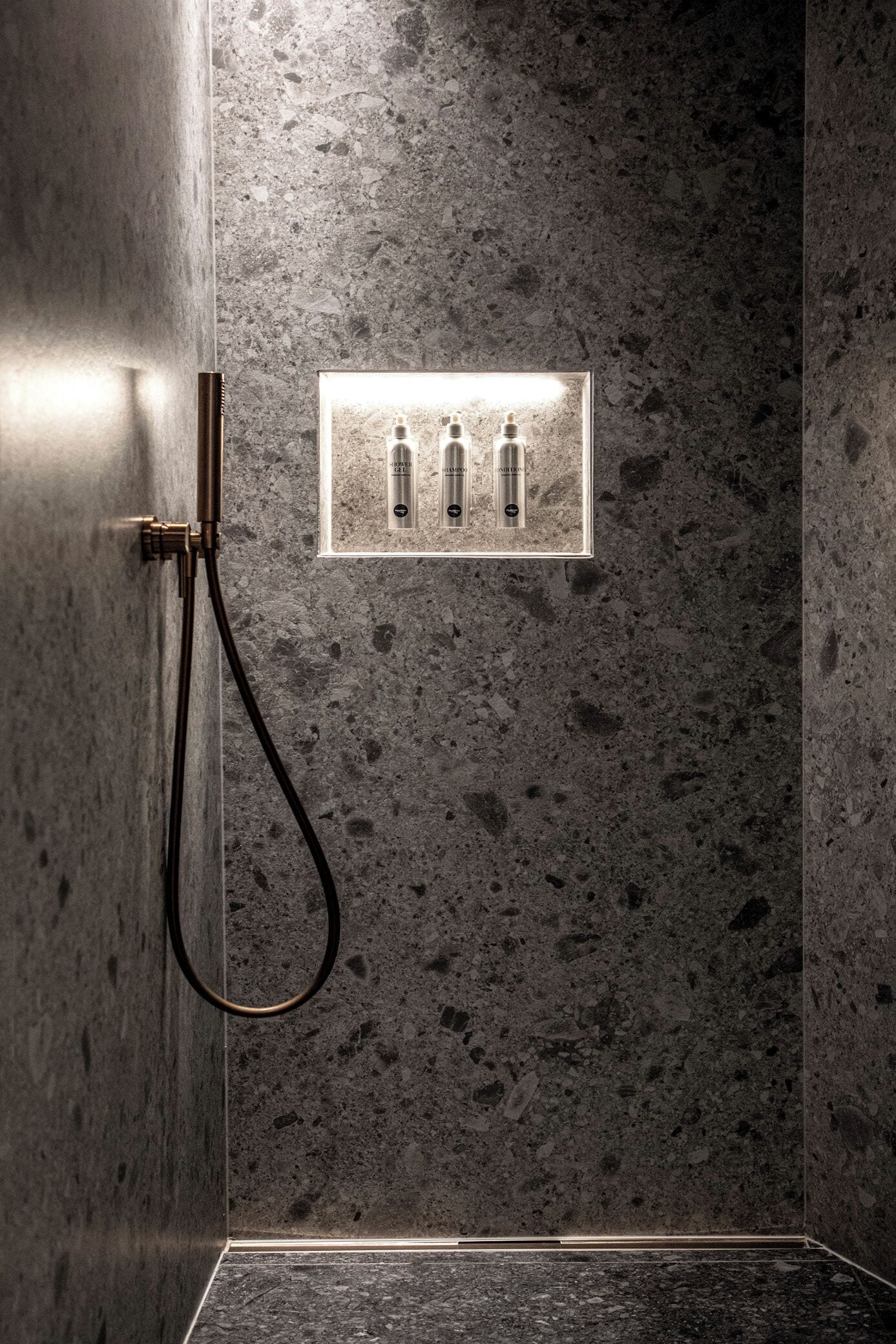 A bathroom with a textured wall, a shower with a handheld hose, and a light switch with three buttons.