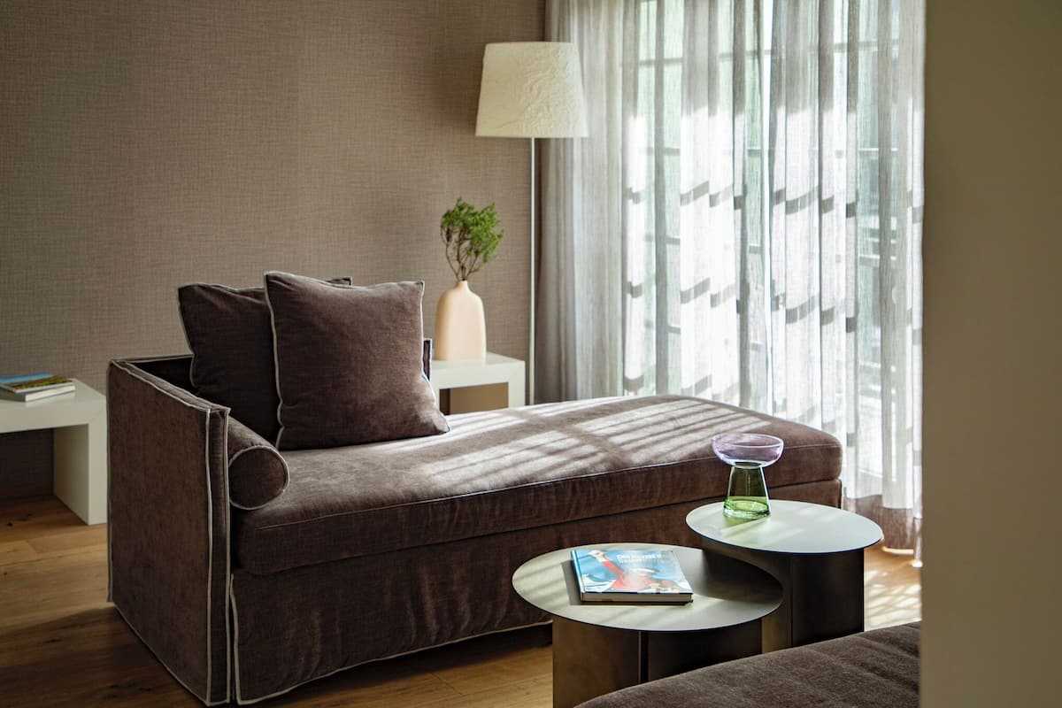 Una sala de estar moderna con un sofá, una pequeña mesa redonda, una lámpara y una ventana con cortinas.