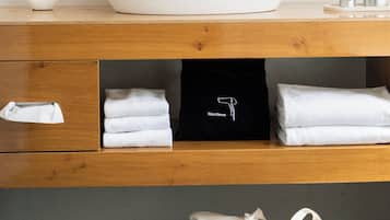 A bathroom with a white vessel sink, wooden vanity, towels, a black bag, and a pair of slippers.
