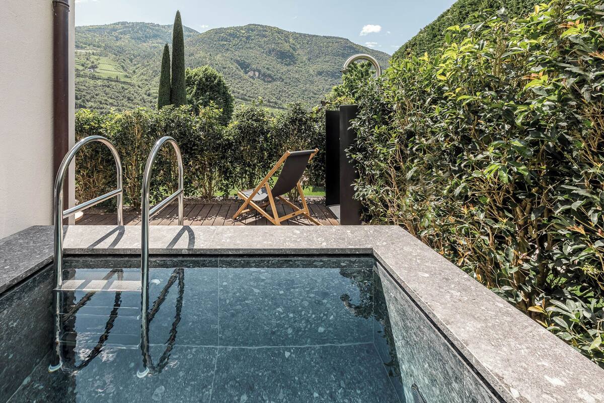 Una piscina con vistas a montañas, una silla y una barandilla metálica.