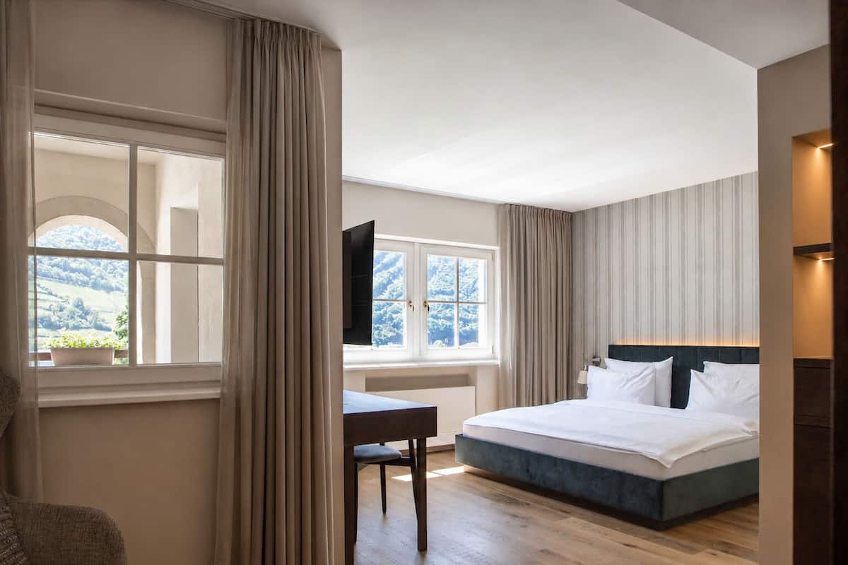 Un dormitorio con cama, escritorio y ventana con cortinas.