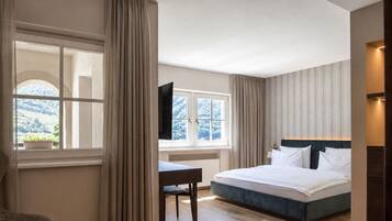 A bedroom with a bed, a desk, and a window with curtains.