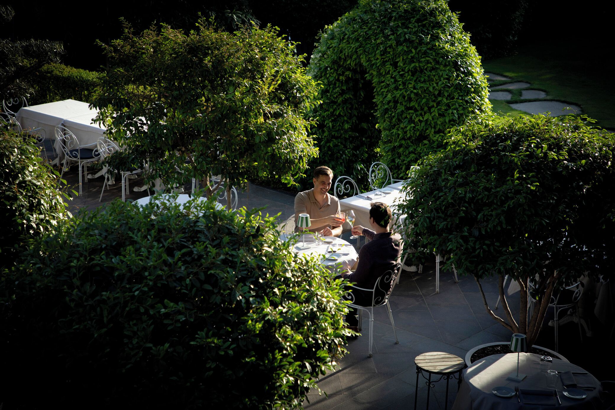 An outdoor dining area with tables and chairs, surrounded by lush greenery and a well-maintained garden.