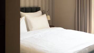 A modern hotel room with a large bed, a headboard, a bedside table with a lamp, and a view of the outdoors through curtains.