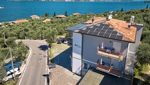 Een modern gebouw met zonnepanelen op het dak, een verharde oprit en een uitzicht op zee en bergen op de achtergrond.