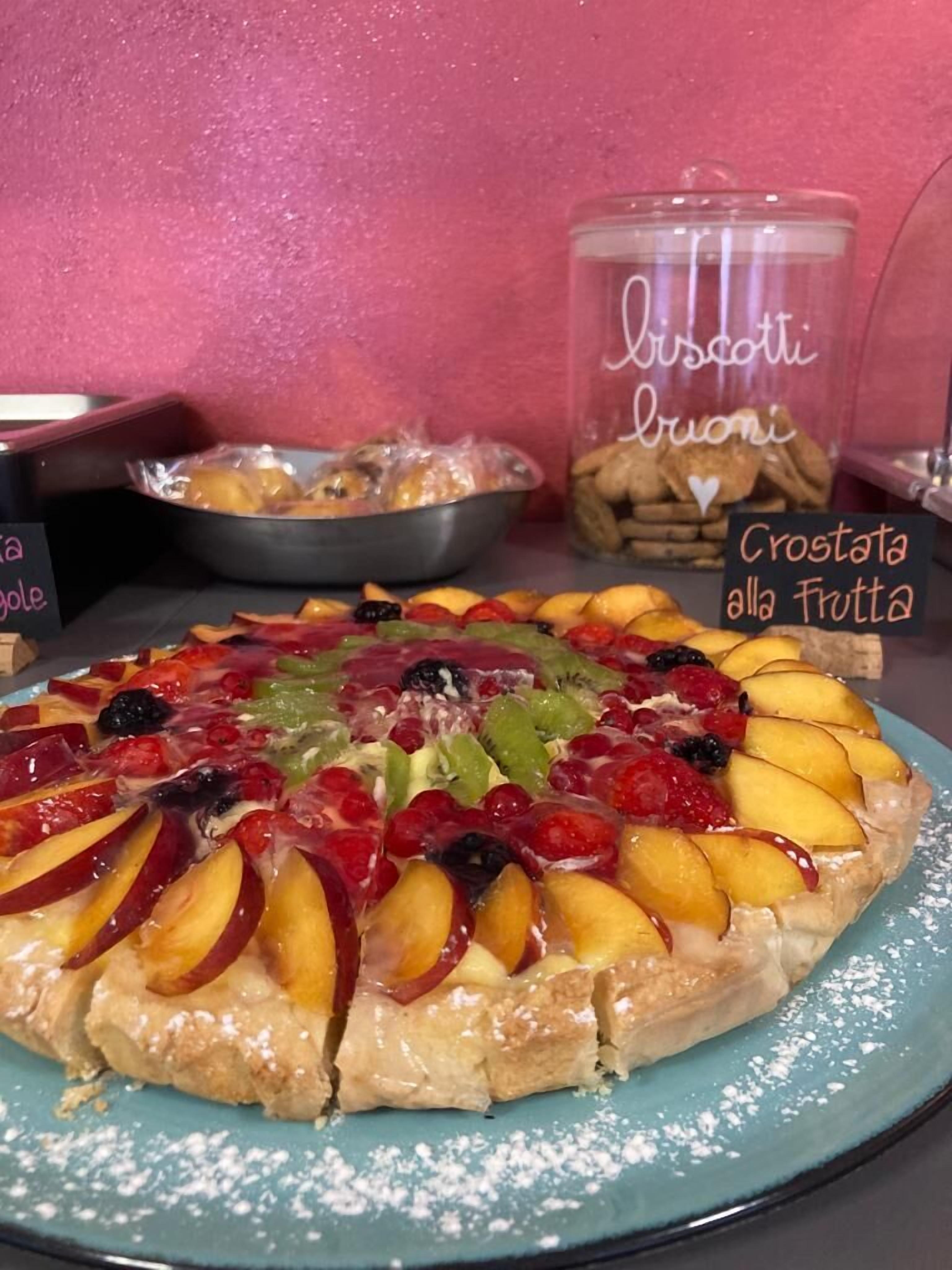 A fruit tart on a blue plate with a sign reading "Crostata alla Fruitta" in the background.