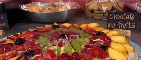 A fruit tart on a blue plate with a sign reading "Crostata alla Fruitta" in the background.
