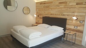 A neatly made bed with white linens, two bedside tables with lamps, and a wooden wall paneling. - Hotel Anna (Malcesine)