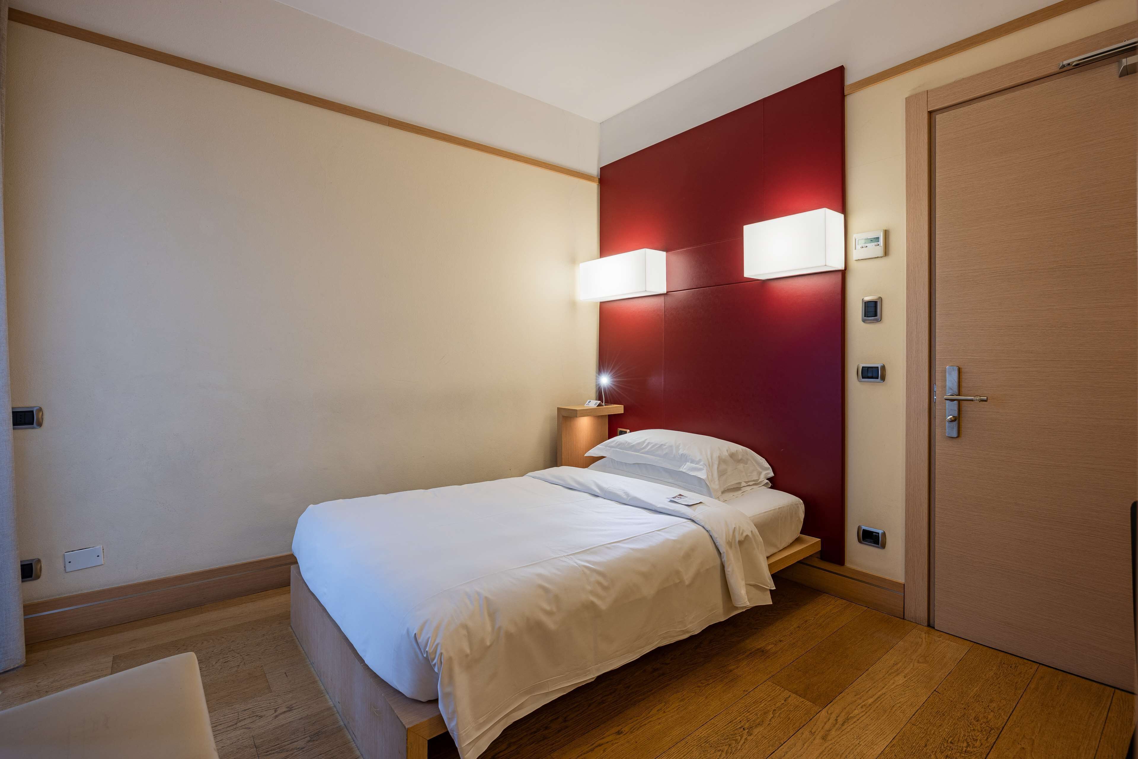 Una camera d'albergo con un letto, comodini, una parete decorata di rosso e una porta in legno.