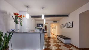Zona de recepción con mostrador de registro, una planta en maceta, un banco y piso a cuadros.