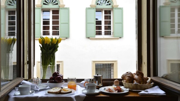 Una mesa de desayuno con un florero, una cafetera y un cesto de cruasanes.