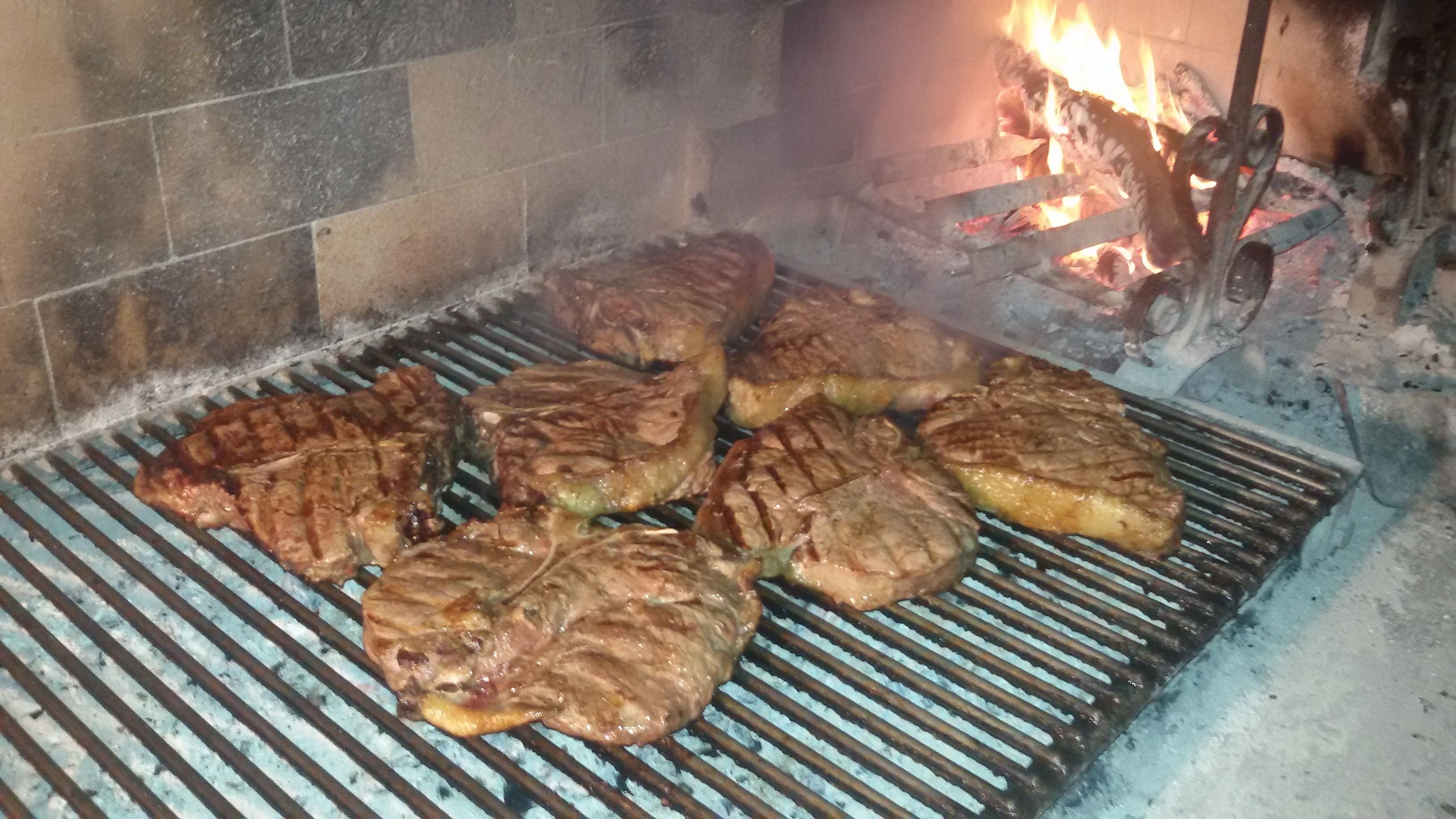 Bistecs a la parrilla sobre una rejilla metálica al fuego abierto.
