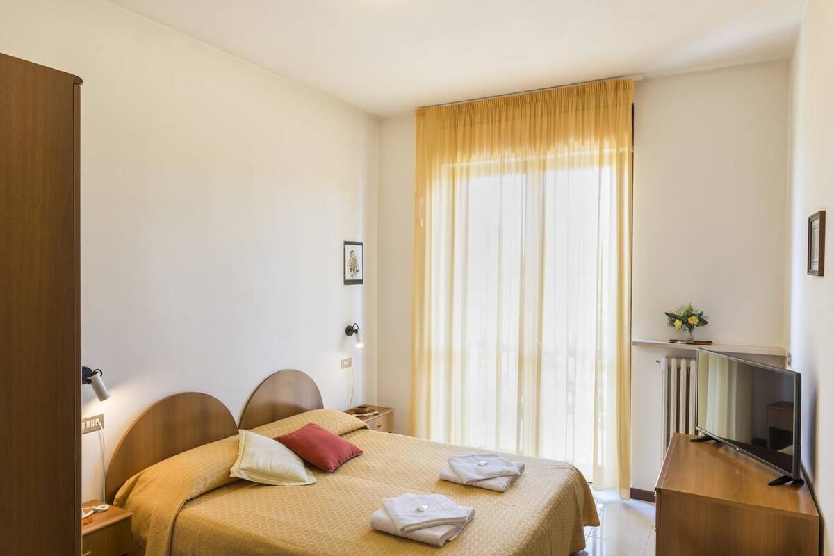 A hotel room with a bed, bedside table, lamp, TV, and curtains.