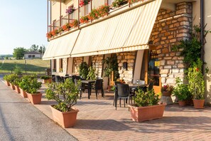 An outdoor seating area with terracotta planters, stone walls, and a metal awning. - Cristina (Rovere Veronese)