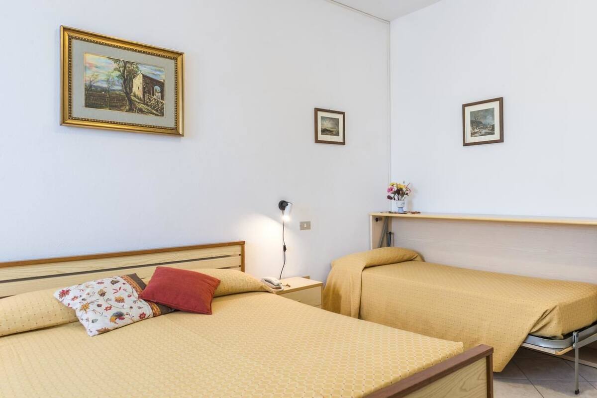 A bedroom with two beds, a nightstand, a lamp, and two framed pictures on the wall.