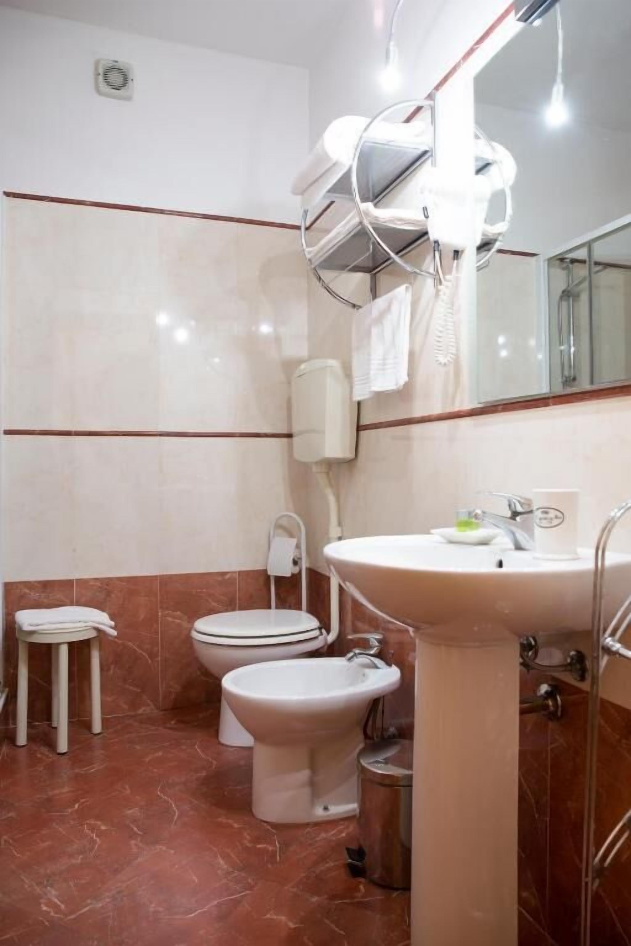 A bathroom with a toilet, bidet, sink, and a hairdryer mounted on the wall.