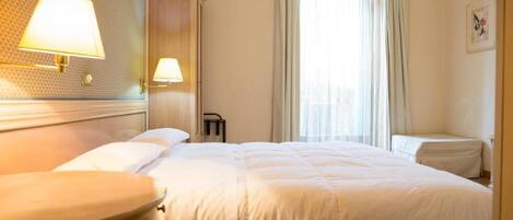 Una habitación de hotel con una cama grande, dos lámparas de noche, una ventana con cortinas y una lámpara de pared.