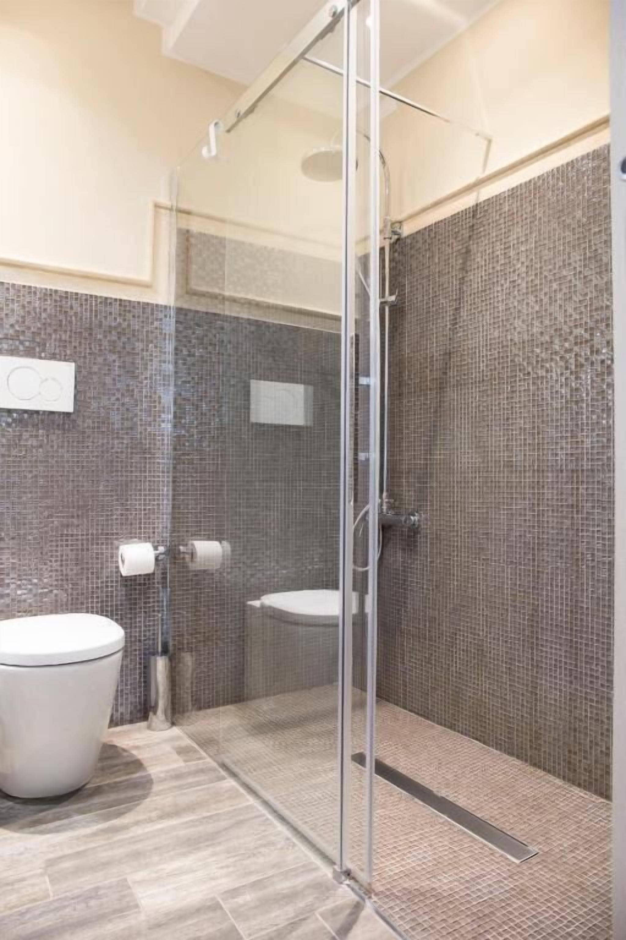 A modern bathroom with a glass shower enclosure, a toilet, and a bidet.