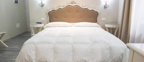Una cama bien hecha con un cabecero acolchado, dos mesitas de noche y lámparas fijadas a la pared.