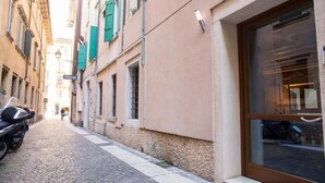 A narrow cobblestone street with buildings on either side, a motorcycle parked on the left, and a large window on the right. - Hotel al Castello (Verona)