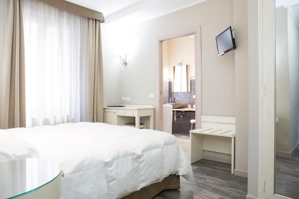 A hotel room with a bed, a desk, a chair, a TV, and a bathroom visible through an open door.