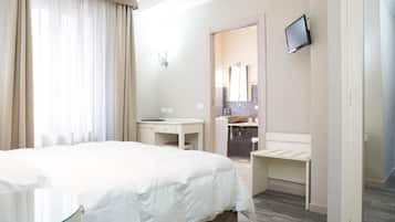Una camera d'albergo con un letto, una scrivania, una sedia, una TV e un bagno visibile attraverso una porta aperta.