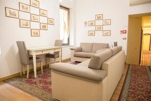 Un salon avec un canapé, une table à manger et des chaises, ainsi qu’un petit bureau. Des tableaux encadrés ornent les murs.