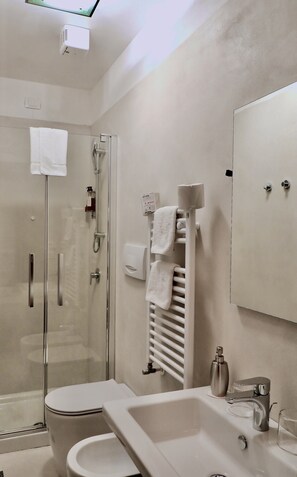 Un baño moderno con ducha envuelta en vidrio, inodoro blanco, lavamanos con espejo y un perchero para toallas.