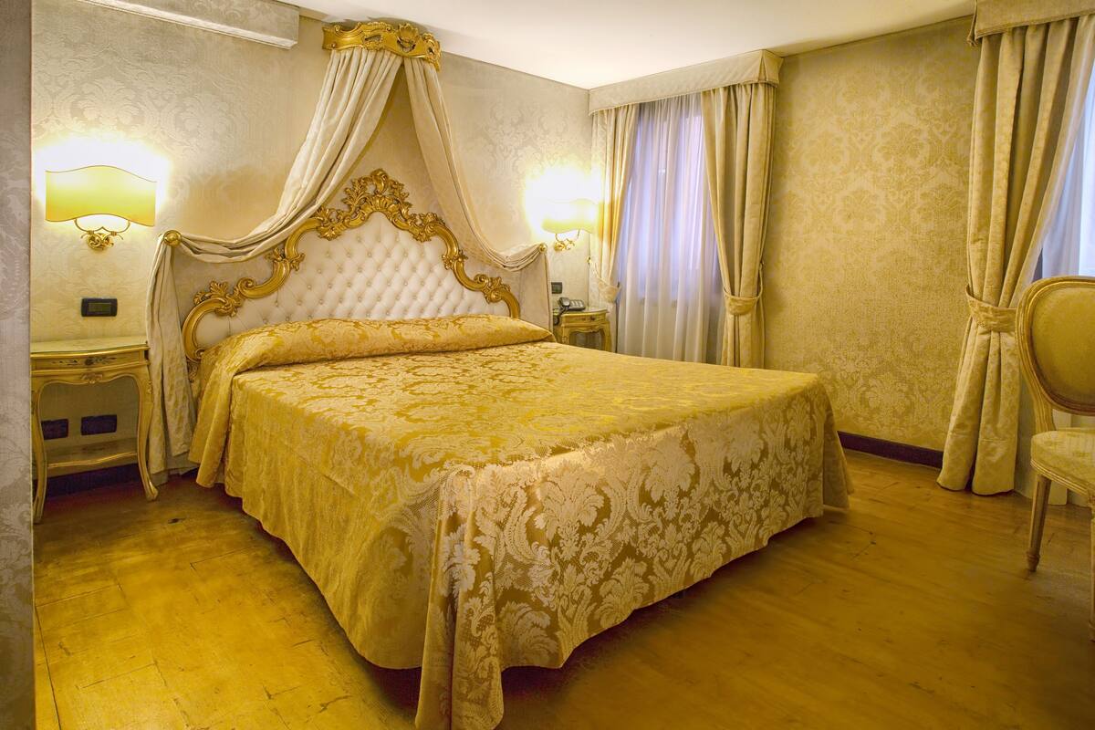 A large, ornate bed with a canopy, two bedside tables with lamps, and a chair.