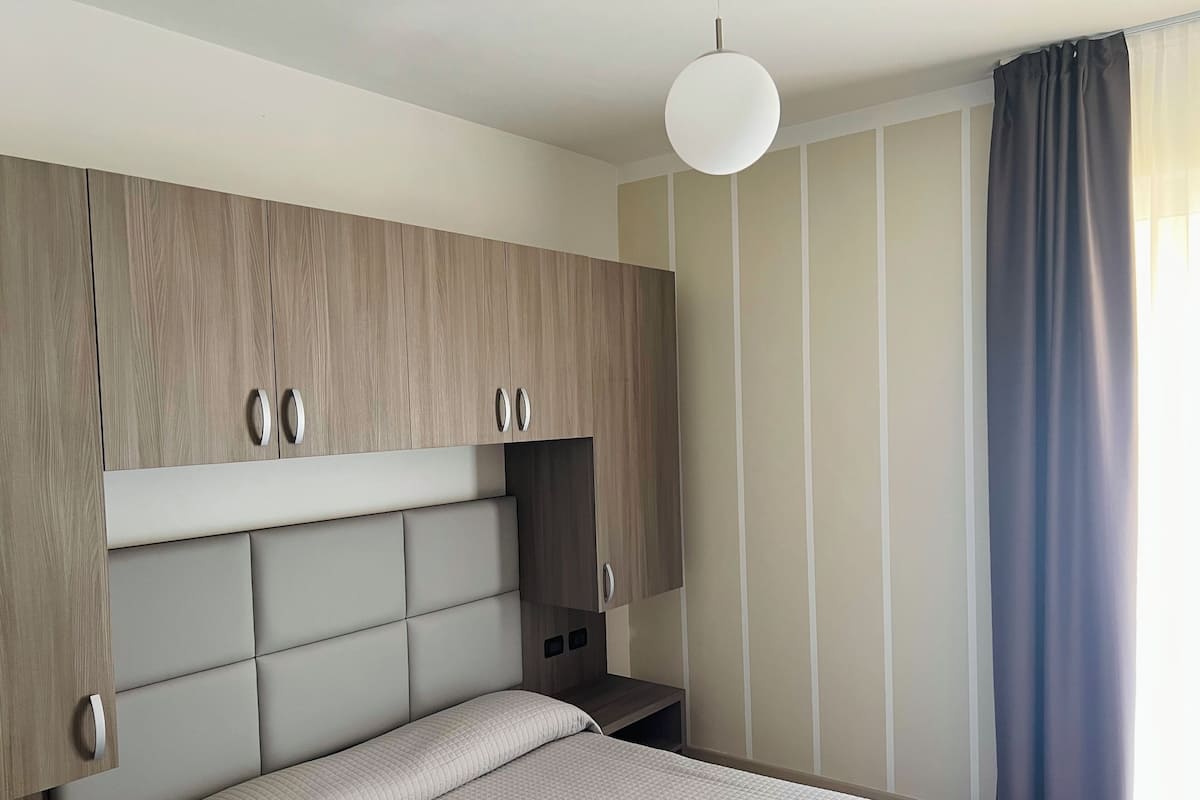 A bedroom with a bed, a wardrobe, and a hanging light fixture.
