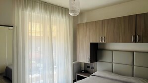 Une chambre à coucher moderne, avec un lit, une table de chevet, une armoire et des rideaux légers.