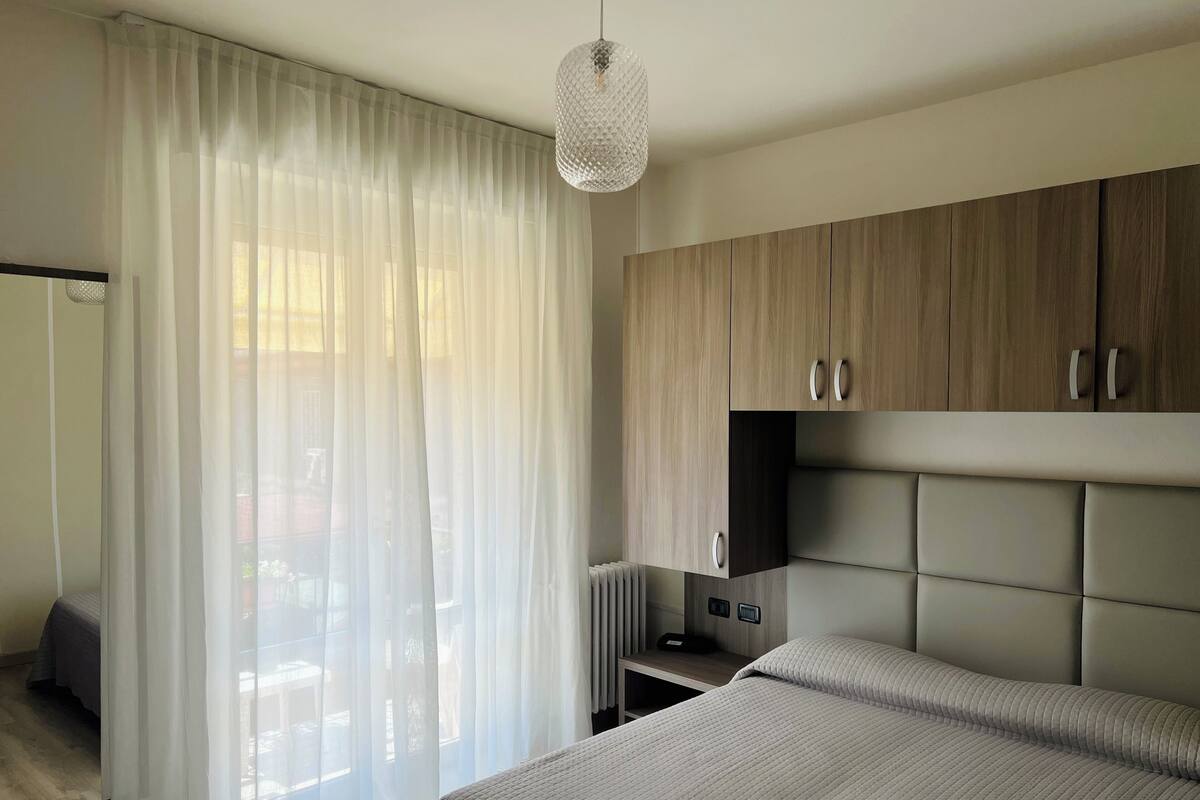 A modern bedroom with a bed, a nightstand, a wardrobe, and sheer curtains.