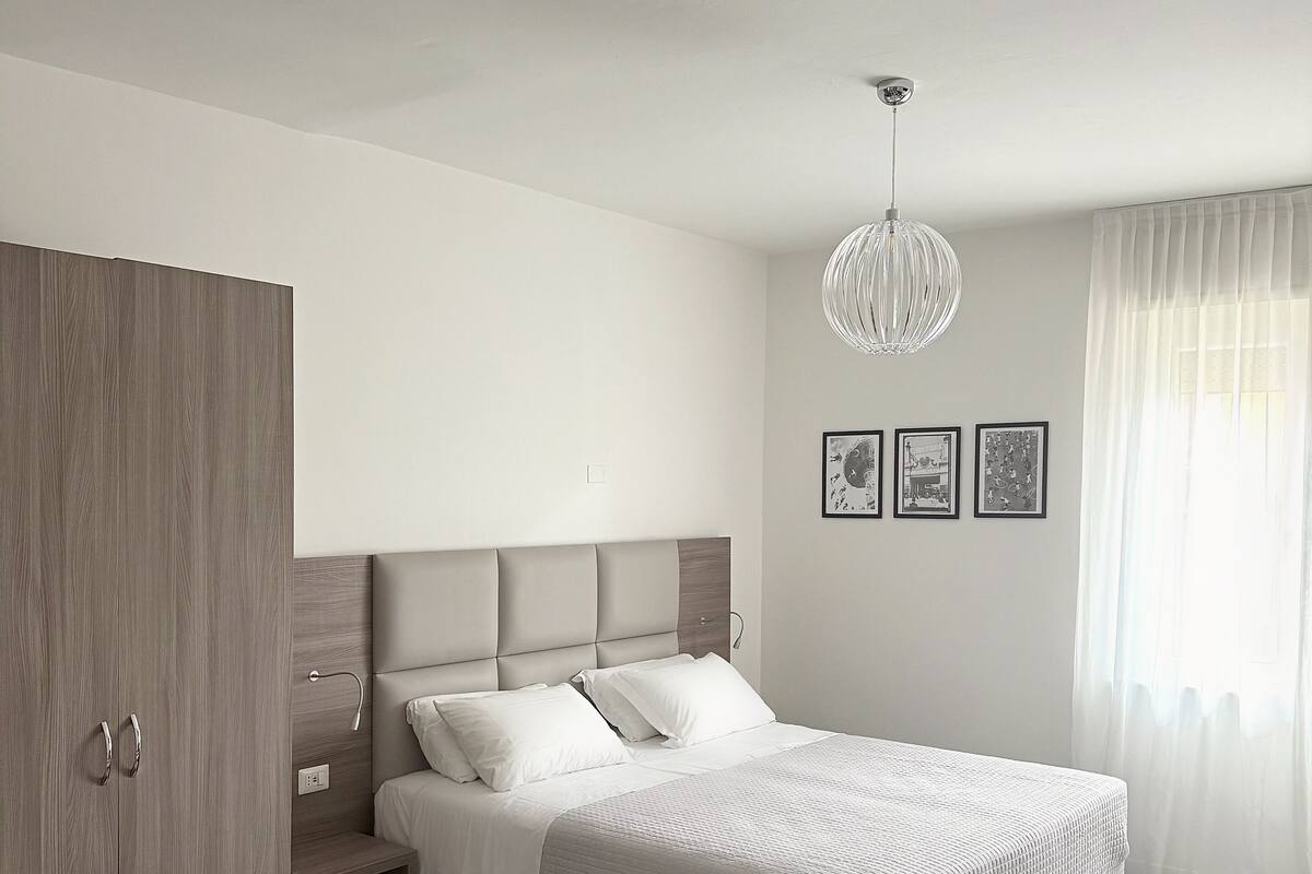 A bedroom with a bed, a wardrobe, a nightstand, and a chandelier.