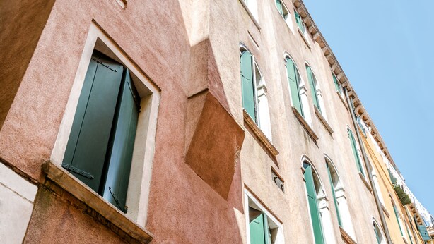 Une façade d’immeuble avec de nombreuses fenêtres, dont certaines sont dotées de volets, et un ciel dégagé en arrière-plan.