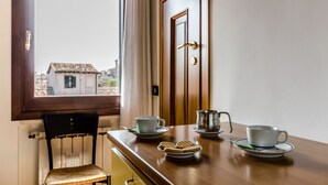 Une pièce avec une table en bois mise pour le thé, une chaise, une fenêtre donnant sur des immeubles et une porte.