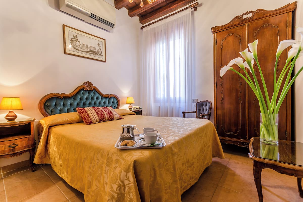 A hotel room with a large bed, two bedside lamps, a wooden wardrobe, and a vase of flowers.
