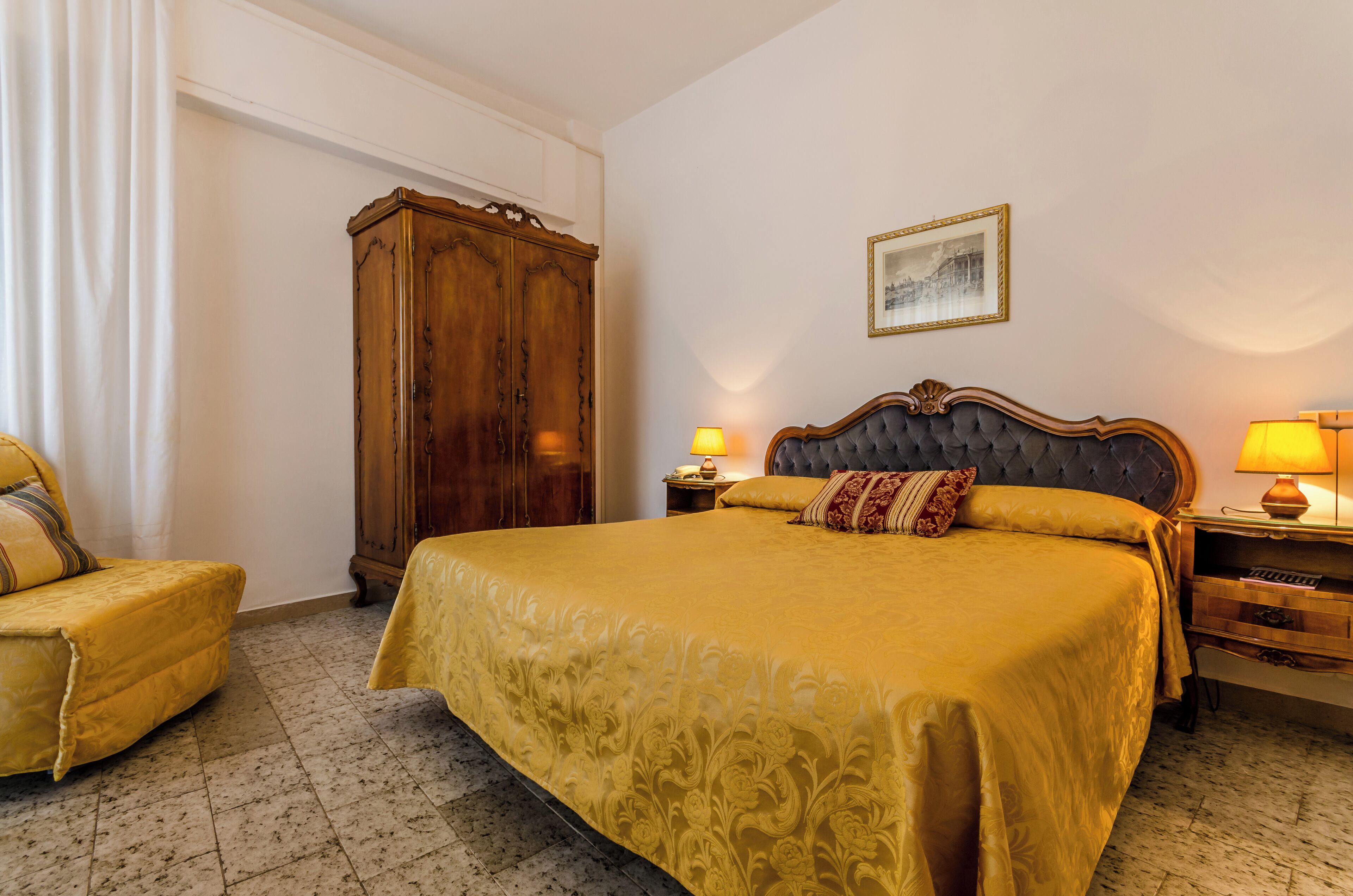 Una habitación de hotel con una cama grande, un armario de madera, una mesita de noche con lámpara y una silla.