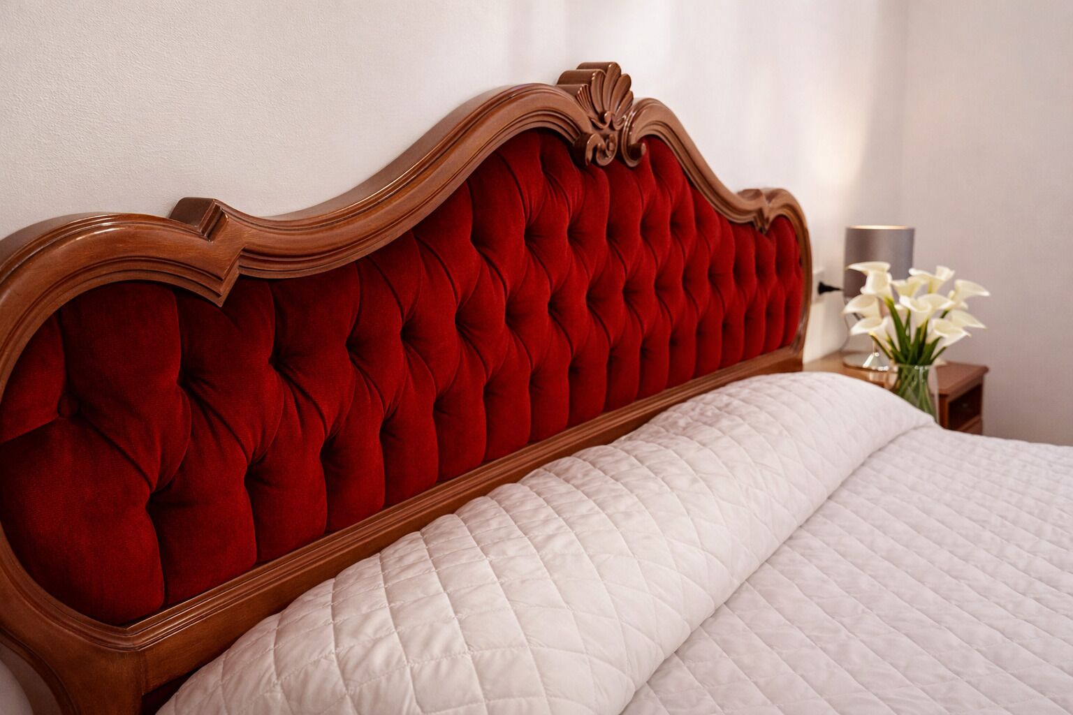 A bed with a red upholstered headboard and a white quilted bedspread.