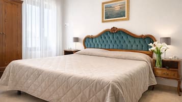 A neatly made bed with a quilted bedspread, a wooden headboard, and a nightstand with a lamp and a vase of flowers.