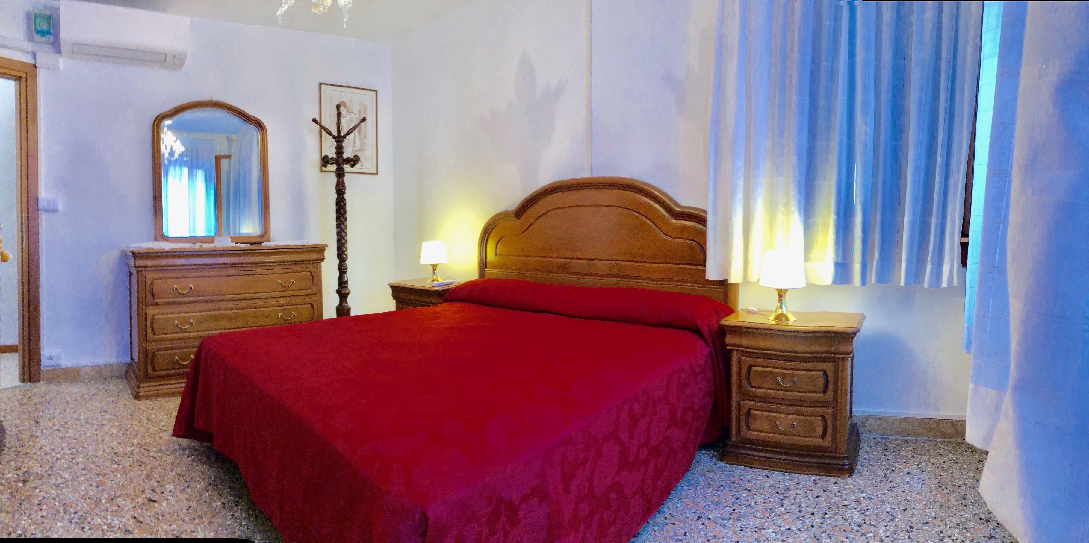 Un dormitorio con una cama grande, mesitas de noche de madera, un aparador, un espejo y una lámpara.