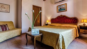 Une chambre d’hôtel avec un lit, un canapé, une petite table avec un ordinateur portable, un vase de fleurs et un tableau au mur.