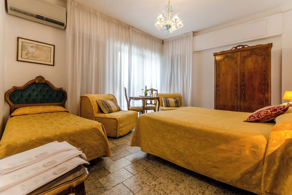 A hotel room with two beds, a wooden wardrobe, a chair, a small table, and a chandelier.