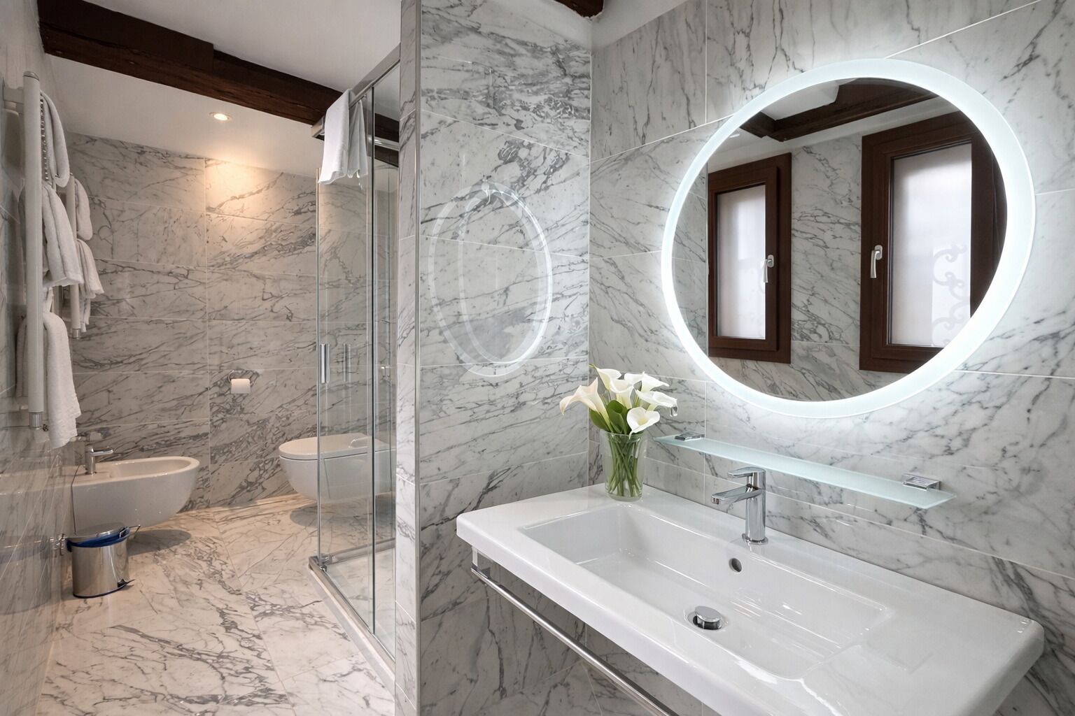 A modern bathroom with a glass shower enclosure, a white sink, and a marble-tiled wall.